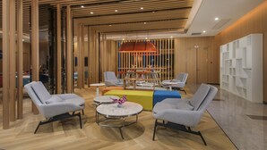 Un hall d’entrée moderne avec un plafond à lattes en bois, des fauteuils gris, une table centrale ornée d’un vase de fleurs et une étagère blanche.