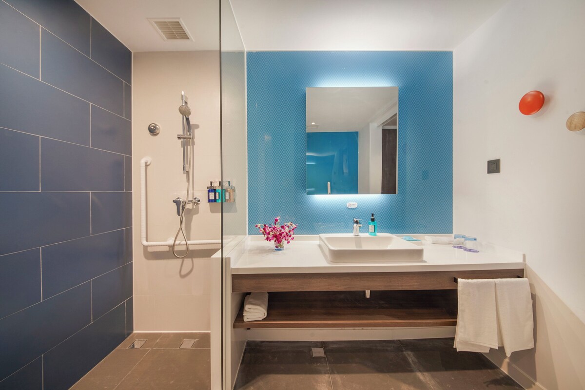 Un baño moderno con cabina de ducha de vidrio, lavamanos blanco y espejo con una pared de acento azul.