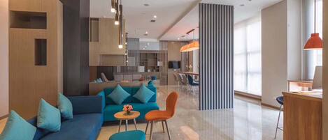 A modern living area with a sofa, ottoman, and chairs, a dining area with a table and chairs, and a kitchen in the background.