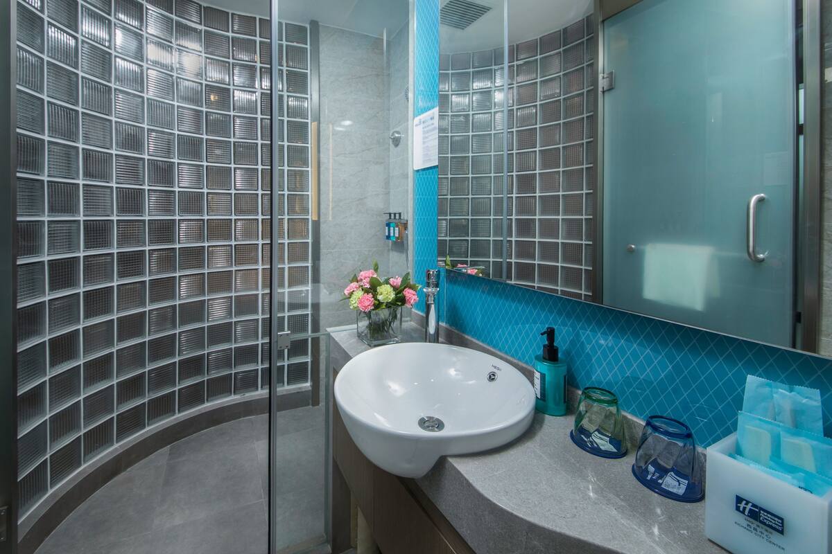 A modern bathroom with a curved glass shower enclosure, a white sink, and a blue-tiled vanity area.