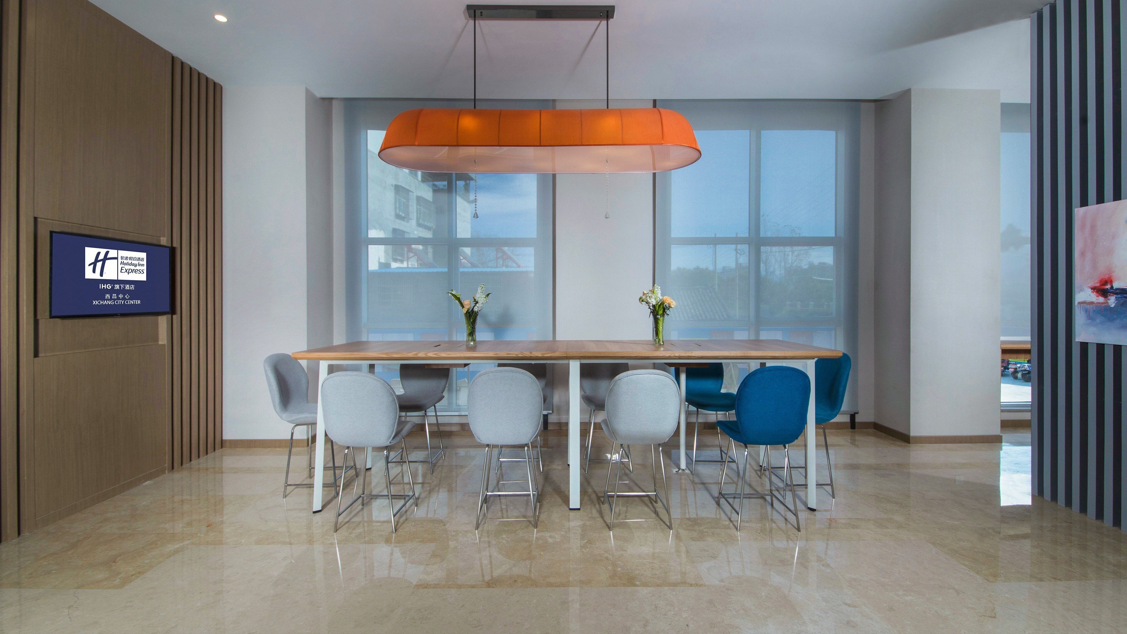 A conference room with a wooden table, six chairs, a large window, and a television screen on the wall.