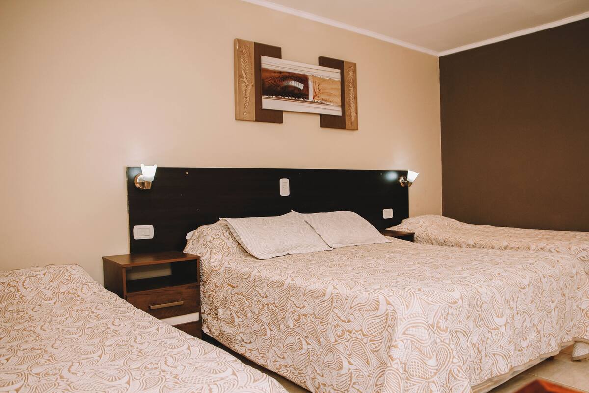 A hotel room with two beds, a nightstand, a framed picture on the wall, and a light switch.