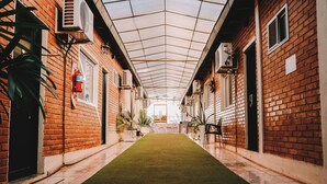 A corridor with a green carpet, brick walls, and air conditioning units. - Altos del Iguazu Hotel (Puerto Iguazú)