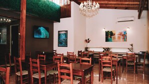 A dining area with wooden tables and chairs, a chandelier, and artwork on the walls. - Altos del Iguazu Hotel (Puerto Iguazú)