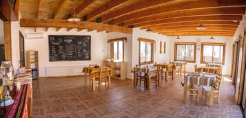 Un comedor con mesas y sillas de madera, un menú en la pizarra y un sistema de buffet.