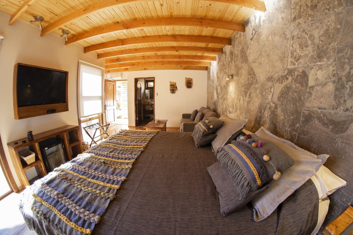 Une pièce spacieuse avec un grand lit, des poutres en bois au plafond, des murs en pierre, un téléviseur à écran plat et une cheminée.