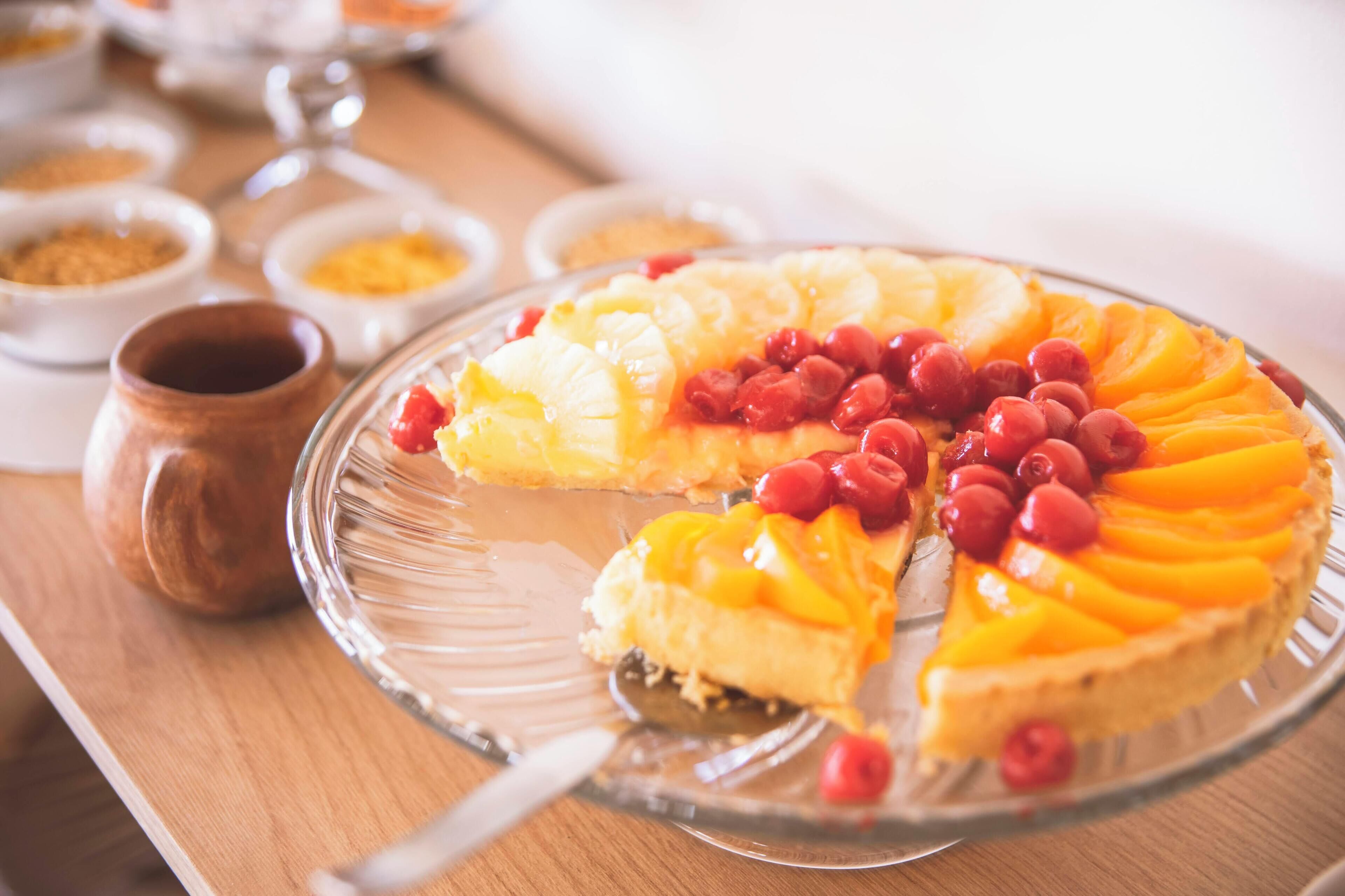 A pie with fruit toppings on a glass plate.