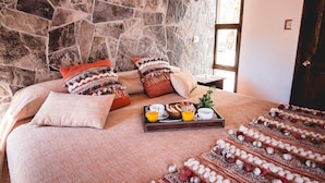 A bed with a stone wall backdrop, a tray with breakfast items, and a window with daylight.