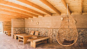A rustic wooden interior with stone walls, a stone bench, and a hanging wicker chair.