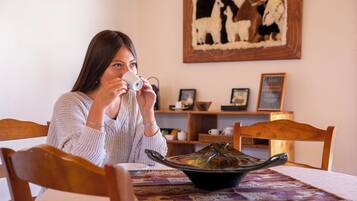 A person sitting at a table with a bowl of food, a framed picture on the wall, and a wooden chair.