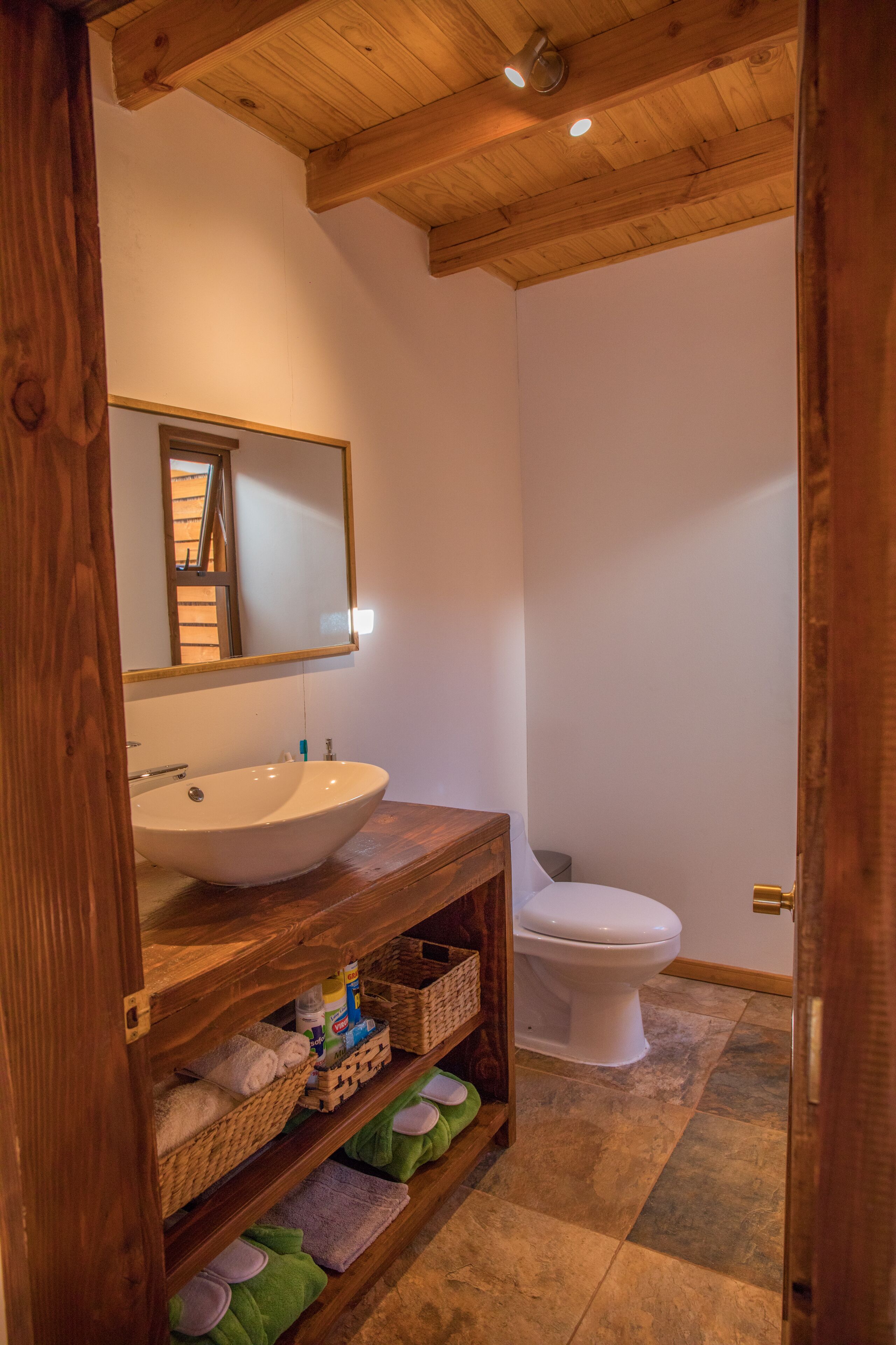 A bathroom with a wooden vanity, a white sink, a mirror, and a toilet.