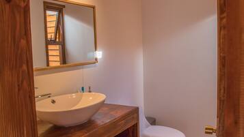 A bathroom with a wooden vanity, a white sink, a mirror, and a toilet.