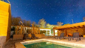 A pool area with lounge chairs and a wooden structure under a starry night sky.