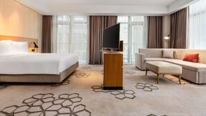 A modern hotel room with a large bed, a sofa, a flat-screen TV on a wooden stand, and a patterned carpet. - Hyatt Place Chongli (Zhangjiakou)