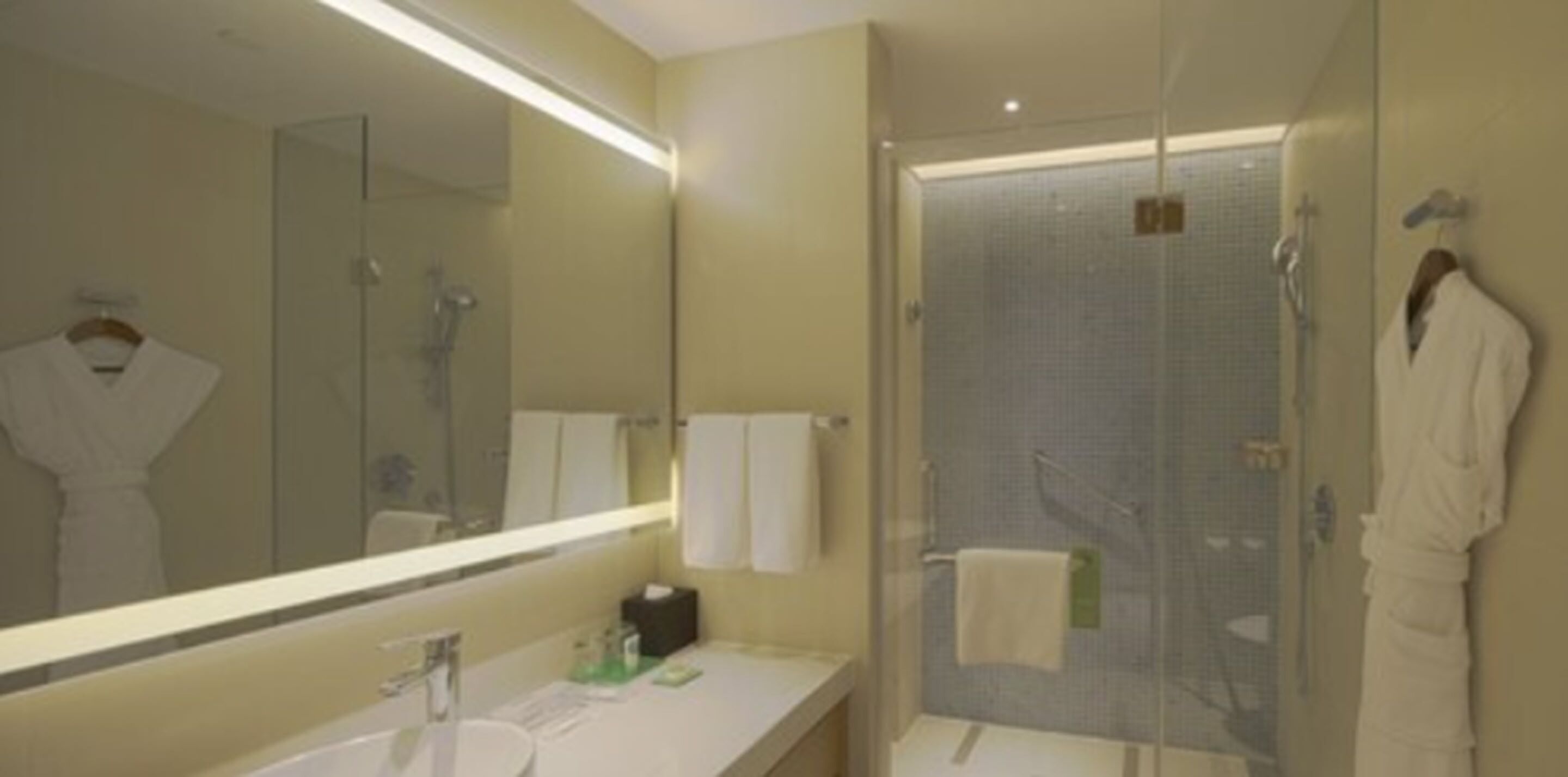 Une salle de bain d’hôtel avec un grand miroir, un lavabo, une douche en verre et une robe accrochée au mur.