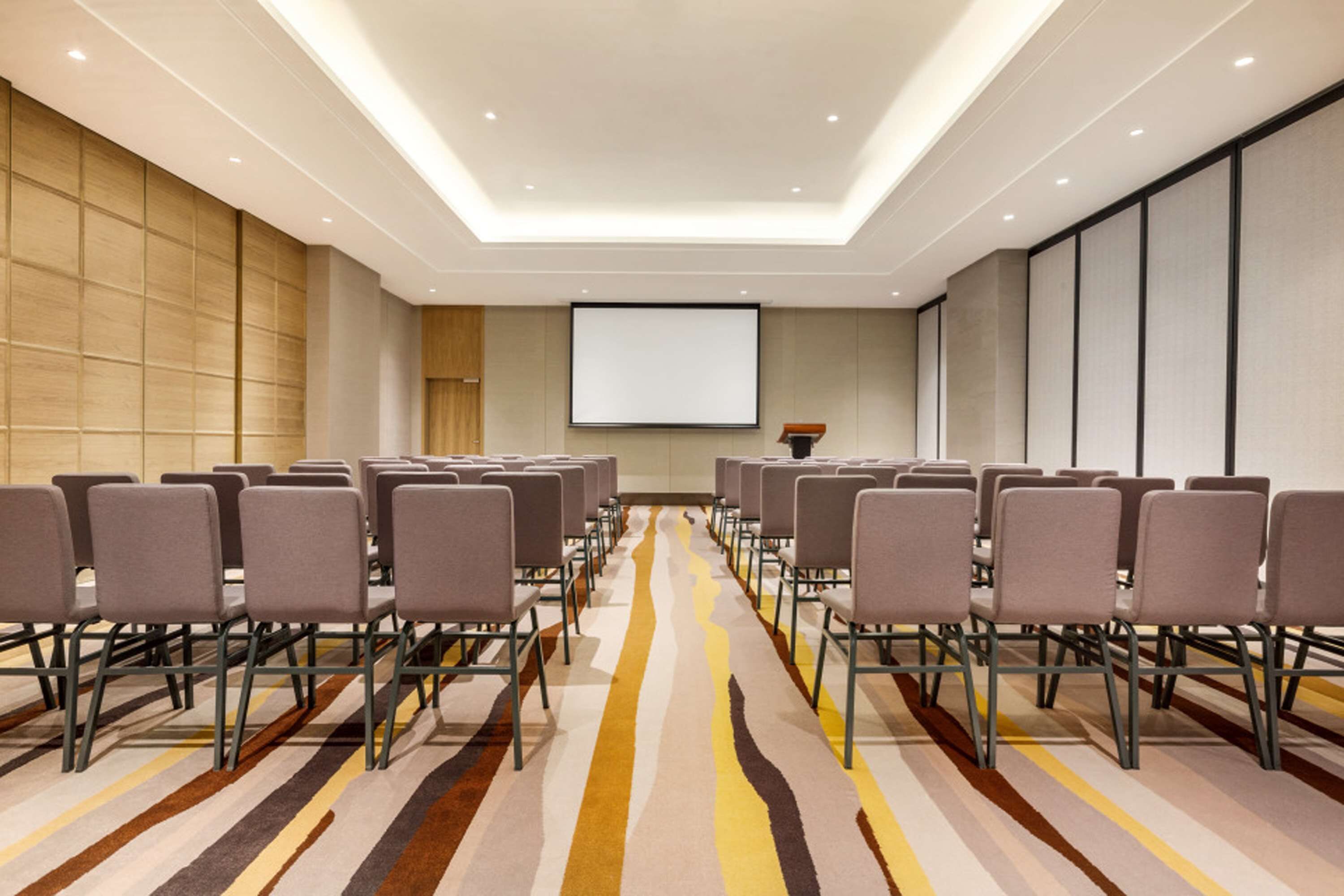 A conference room with rows of chairs, a projector screen, and a patterned carpet.