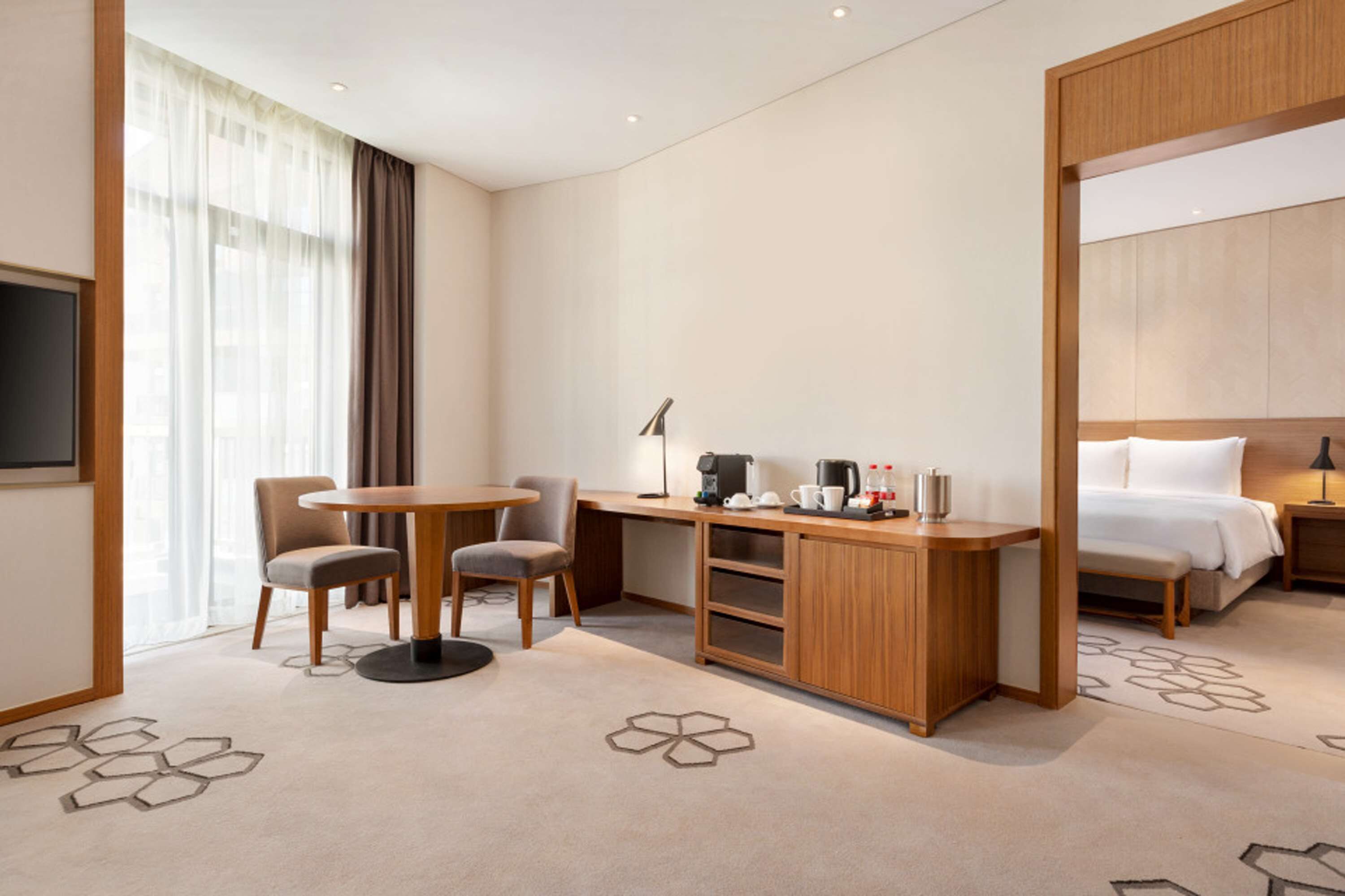 A hotel room with a bed, a desk with a chair, a coffee maker, and a TV.