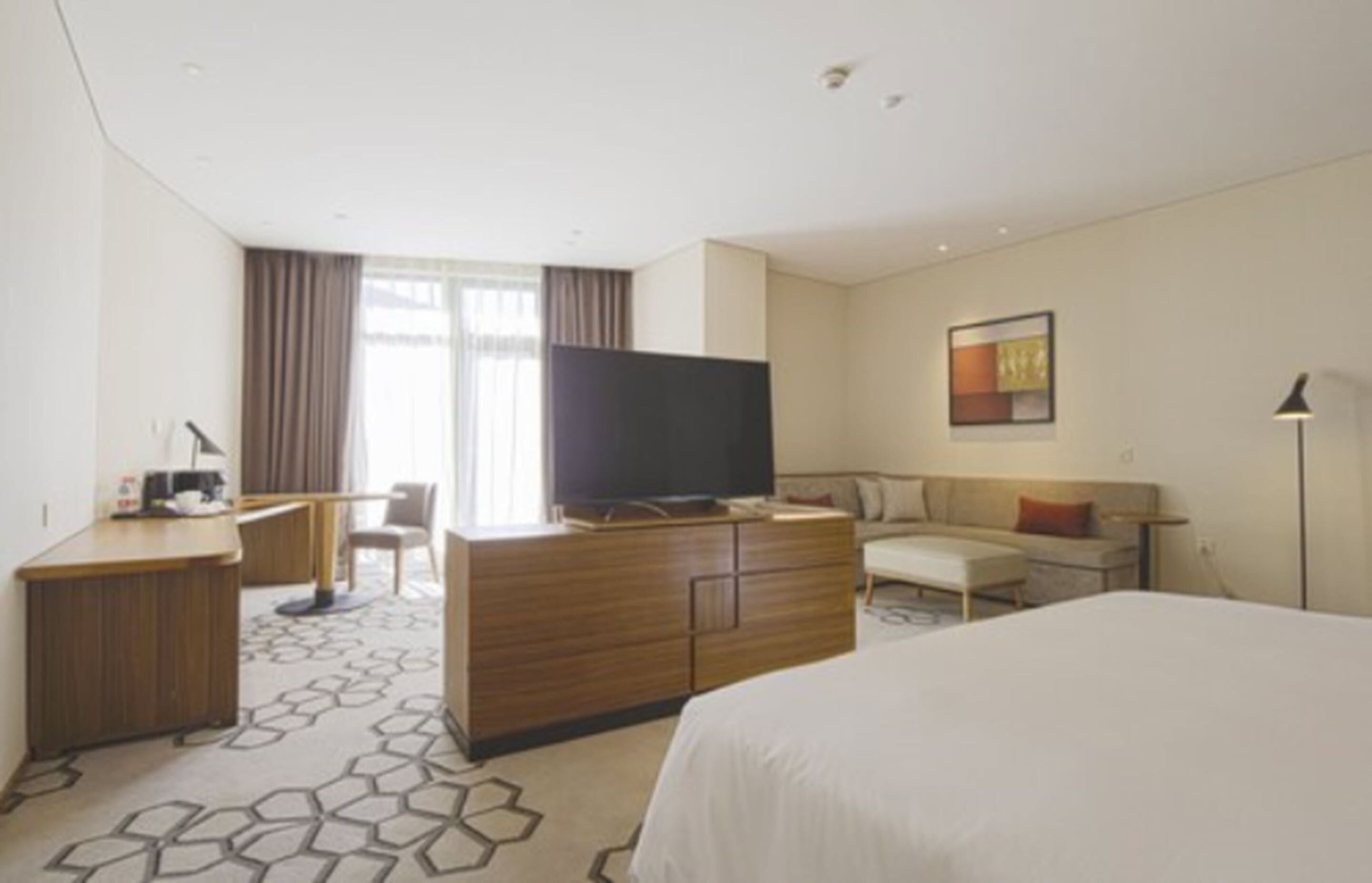 Ein Hotelzimmer mit einem Bett, einem Schreibtisch, einem Fernseher, einer Couch und einer Lampe.