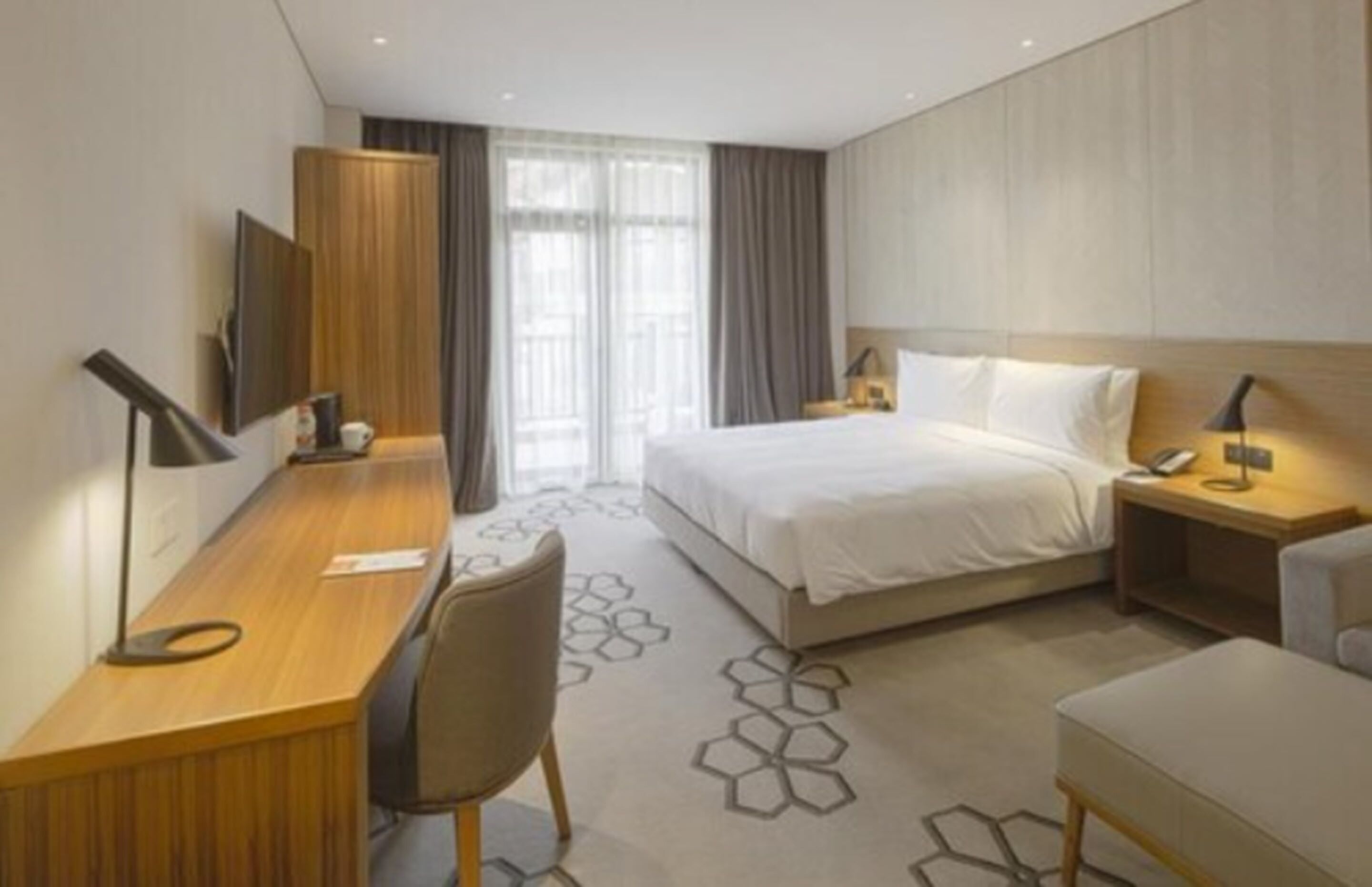 A hotel room with a bed, a desk, a chair, a TV, and a window with curtains.