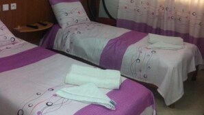 A hotel room with two beds, each with a headboard and a pillow. There is a small table with a remote control on it. - Hôtel Oumaya Safa (Algiers)