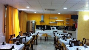 A dining area with tables and chairs, a kitchen in the background, and a yellow wall. - Hôtel Oumaya Safa (Algiers)