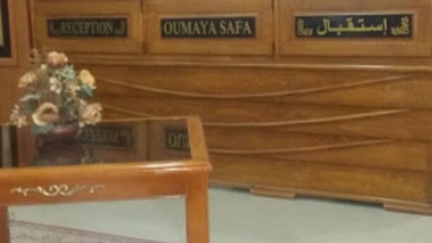 A reception desk with a floral arrangement and a wooden cabinet with signs indicating reception and a safe. - Hôtel Oumaya Safa (Algiers)