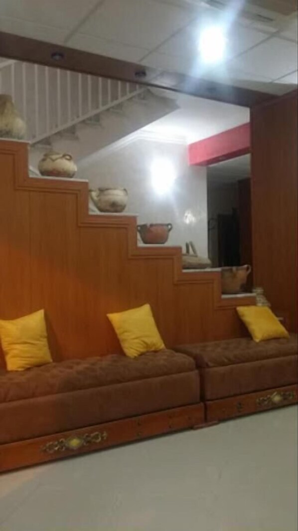 A room with a wooden staircase, a sofa with yellow cushions, and a mirror on the wall.
