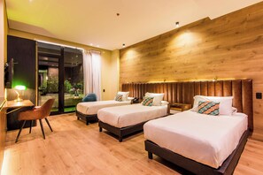 A hotel room with three beds, a desk with a chair, and a large window with curtains.
