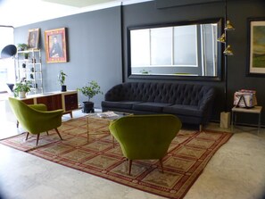 A living room with a dark sofa, two green armchairs, a patterned rug, and a window with blinds. - Viajero Bogota Hostel & Spa (Bogotá)