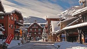 Une rue enneigée bordée d’immeubles, dont un bâtiment rouge doté d’un balcon et un bâtiment en bois dont le toit est recouvert de neige.