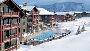 Une station de ski enneigée comprenant plusieurs bâtiments, un espace piscine central et un paysage montagneux en toile de fond.