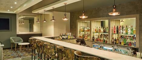 Zona de bar con una barra larga, varios taburetes y una amplia variedad de botellas en estanterías.