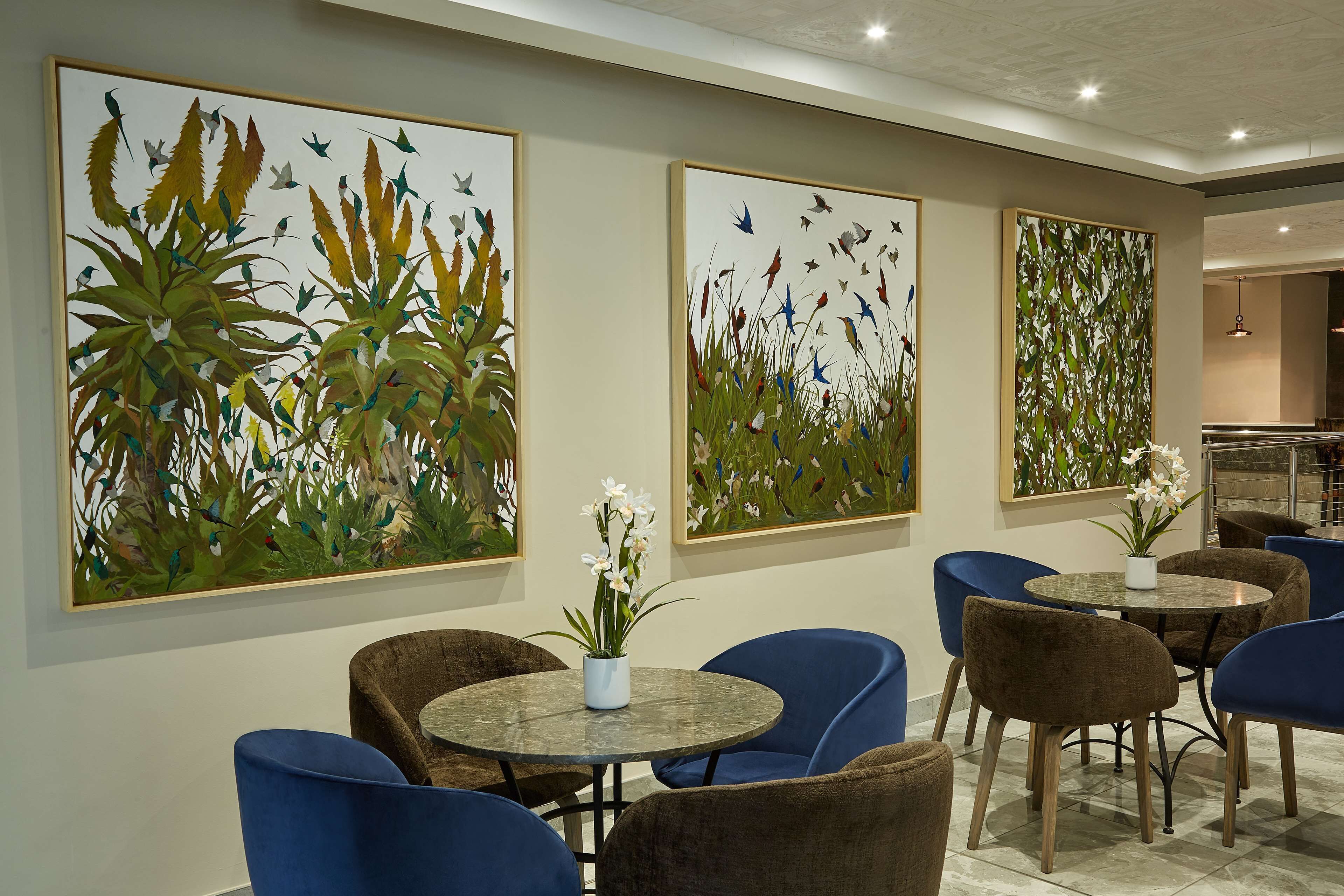 A dining area with round tables and blue chairs, surrounded by large botanical paintings.