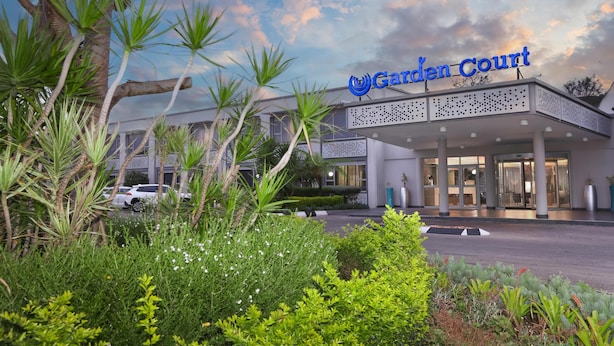 L’entrée d’un hôtel, agrémentée d’une enseigne indiquant « Garden Court », est entourée d’une végétation luxuriante et de palmiers.