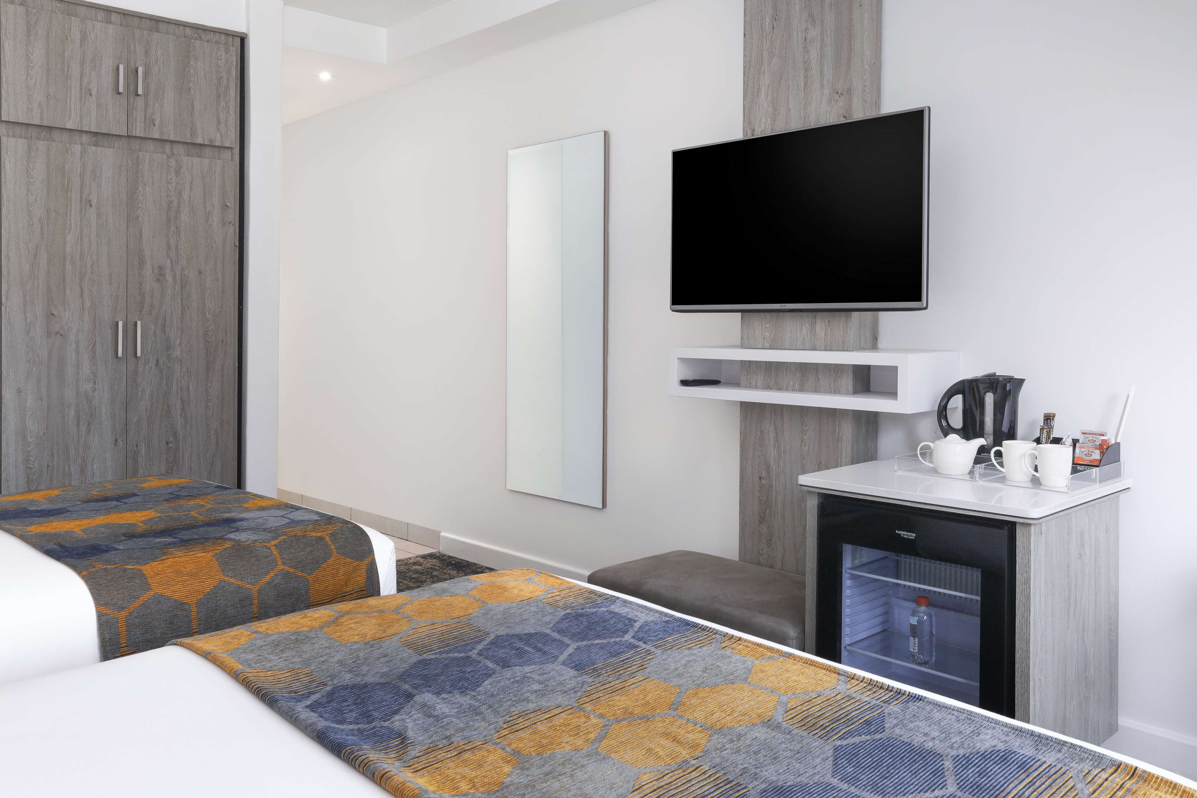 Habitación de hotel con dos camas, televisor, minibar y un espejo grande.