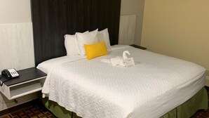 A neatly made bed with white bedding, a green skirt, and a yellow pillow. There is a bedside table with a phone and a lamp. The room has a patterned floor and a headboard with a dark panel. - HomeStay Inn & Suites Edinburg (Edinburg)