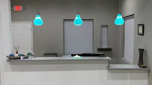 A reception area with a counter, three hanging blue pendant lights, a door, and a small shelf with decorative items. - HomeStay Inn & Suites Edinburg (Edinburg)