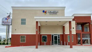 A HomeStay Inn & Suites building with a beige facade, a covered entrance, and a visible American flag. - HomeStay Inn & Suites Edinburg (Edinburg)