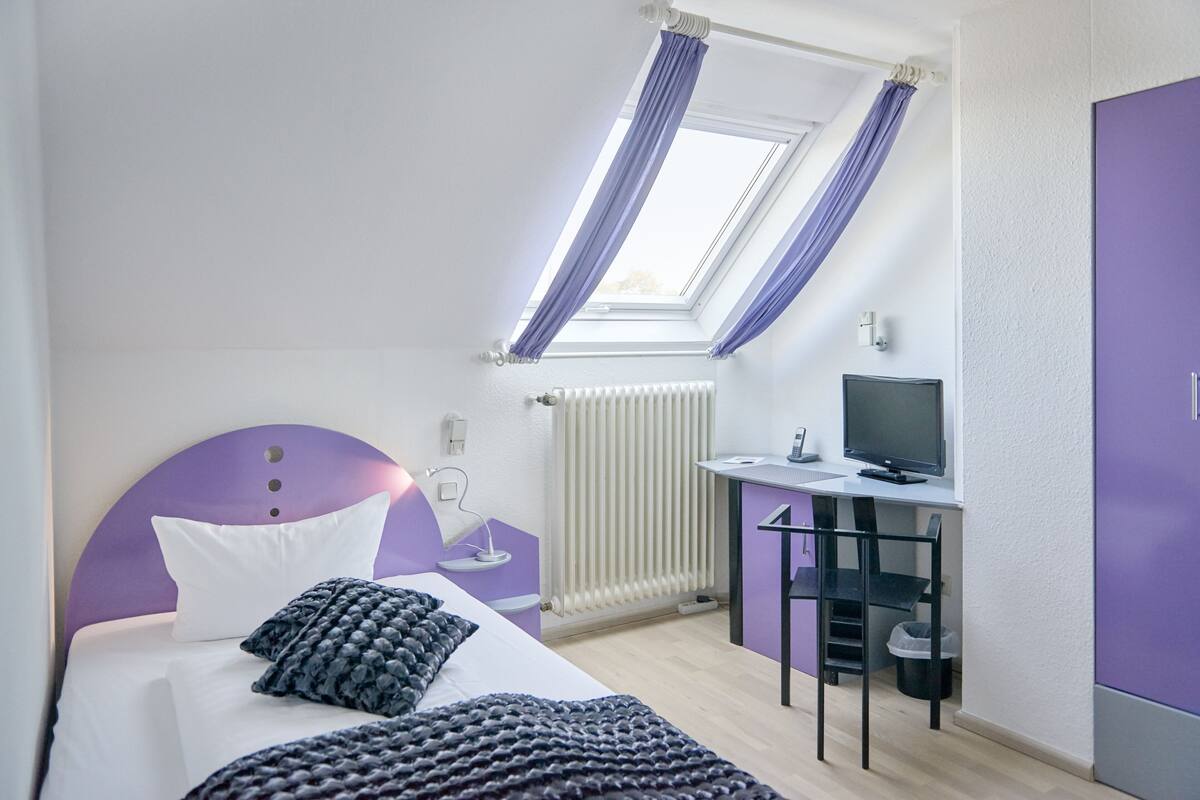A bedroom with a bed, a desk, and a window with curtains.