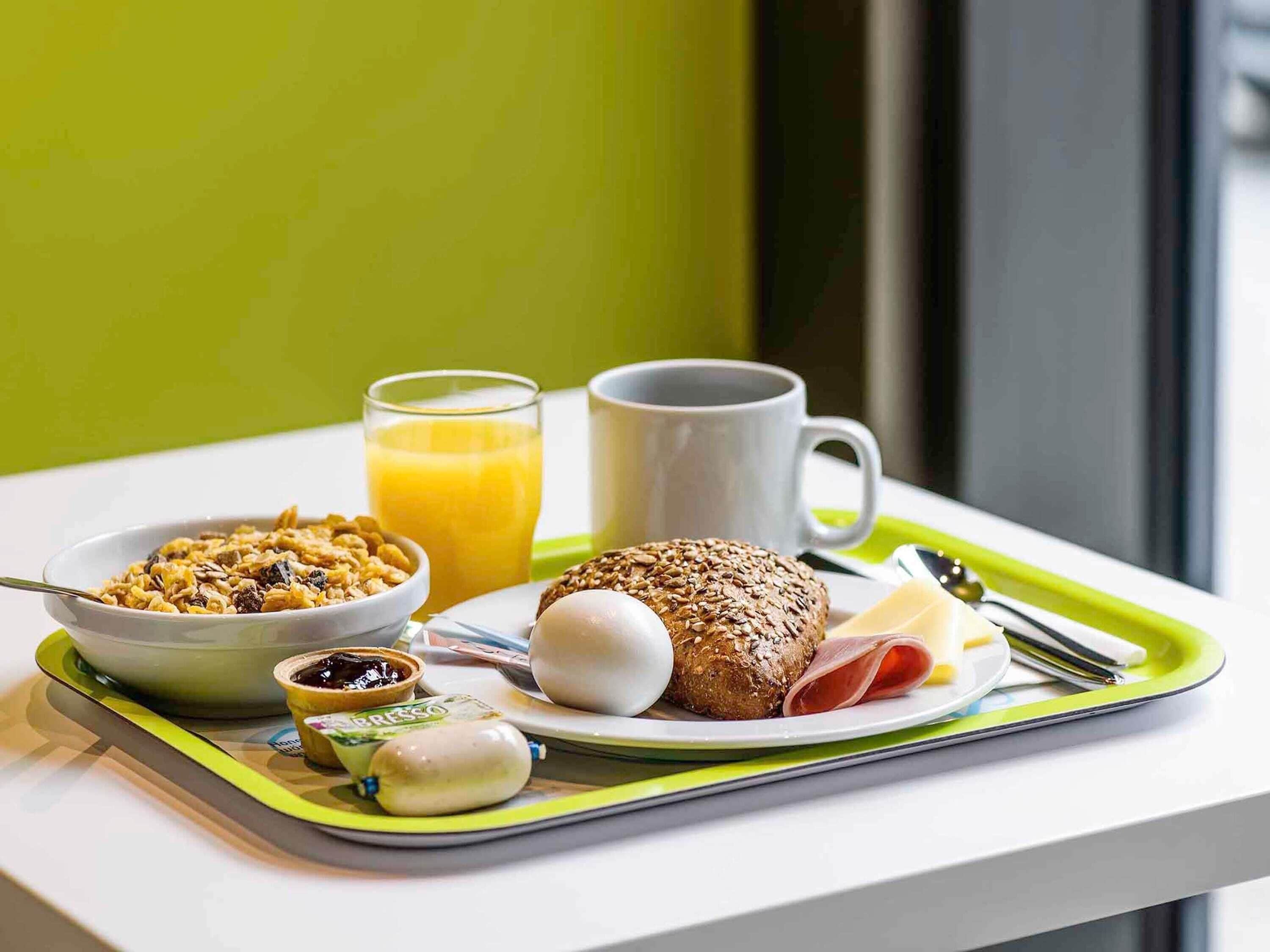 A breakfast tray with cereal, a glass of orange juice, a mug, a slice of bread, a boiled egg, a ham slice, and a small container of jam.