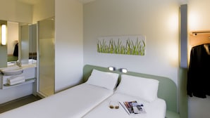 A hotel room with a bed, a bedside table, a mirror, a sink, and a towel rack.