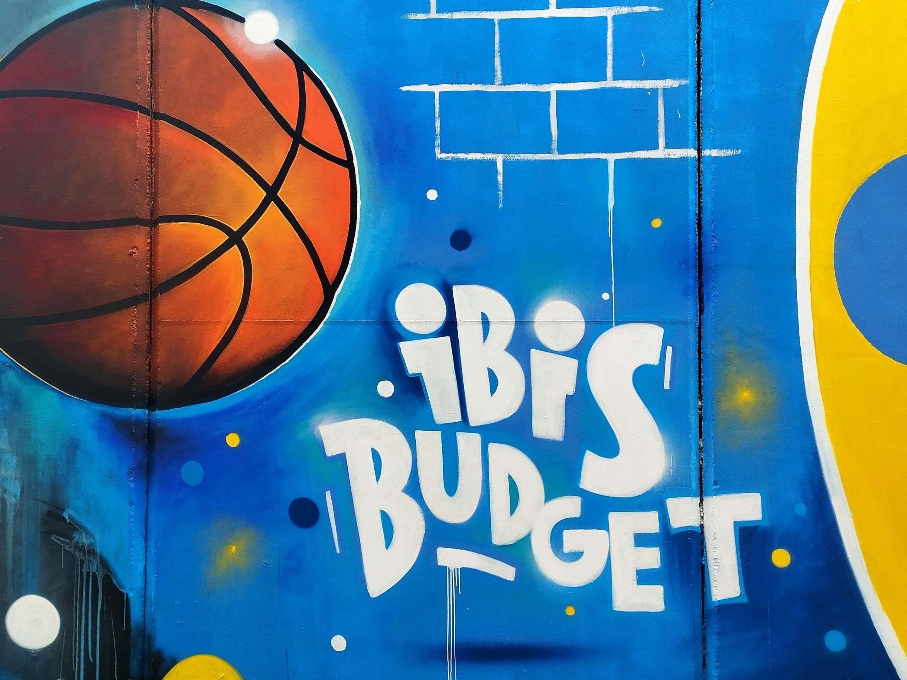 Een muur met graffiti, waaronder een basketbal en de tekst 'IBIS BUDGET'.