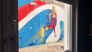 A window with a mural of a person in a red and blue outfit against a cosmic background.