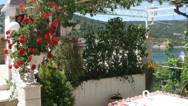 Ein Garten mit einer Pergola, roten Blumen und Blick auf einen Fluss und Hügel im Hintergrund.