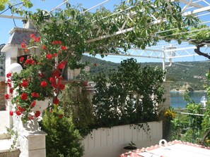 Um jardim com pérgola, flores vermelhas e vista para um rio e colinas ao fundo.