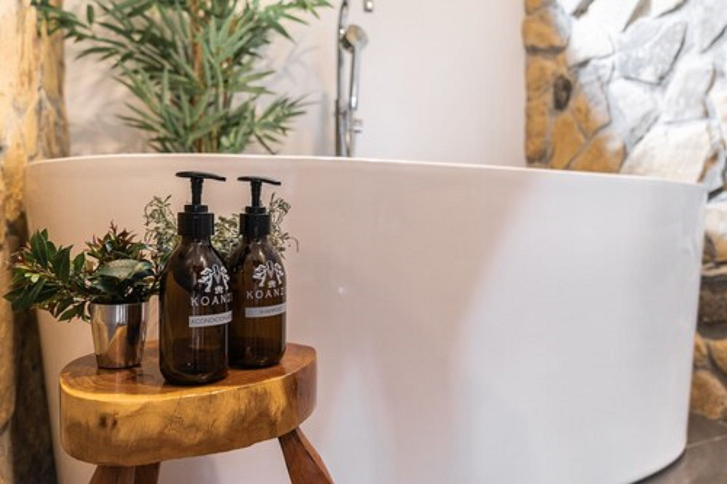 A bathtub with two bottles of 'Koani' on a wooden stool.