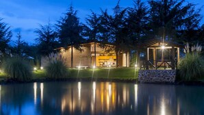 A modern house with a pool, surrounded by trees and featuring a well-lit patio area.