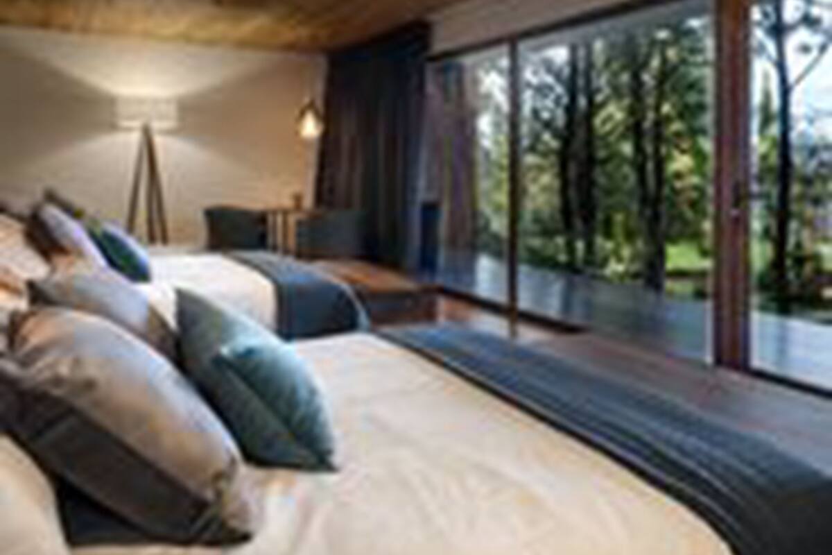 A modern bedroom with a large bed, a desk, and a view of the outdoors.