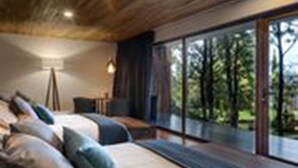 A modern bedroom with a large bed, a desk, and a view of the outdoors.