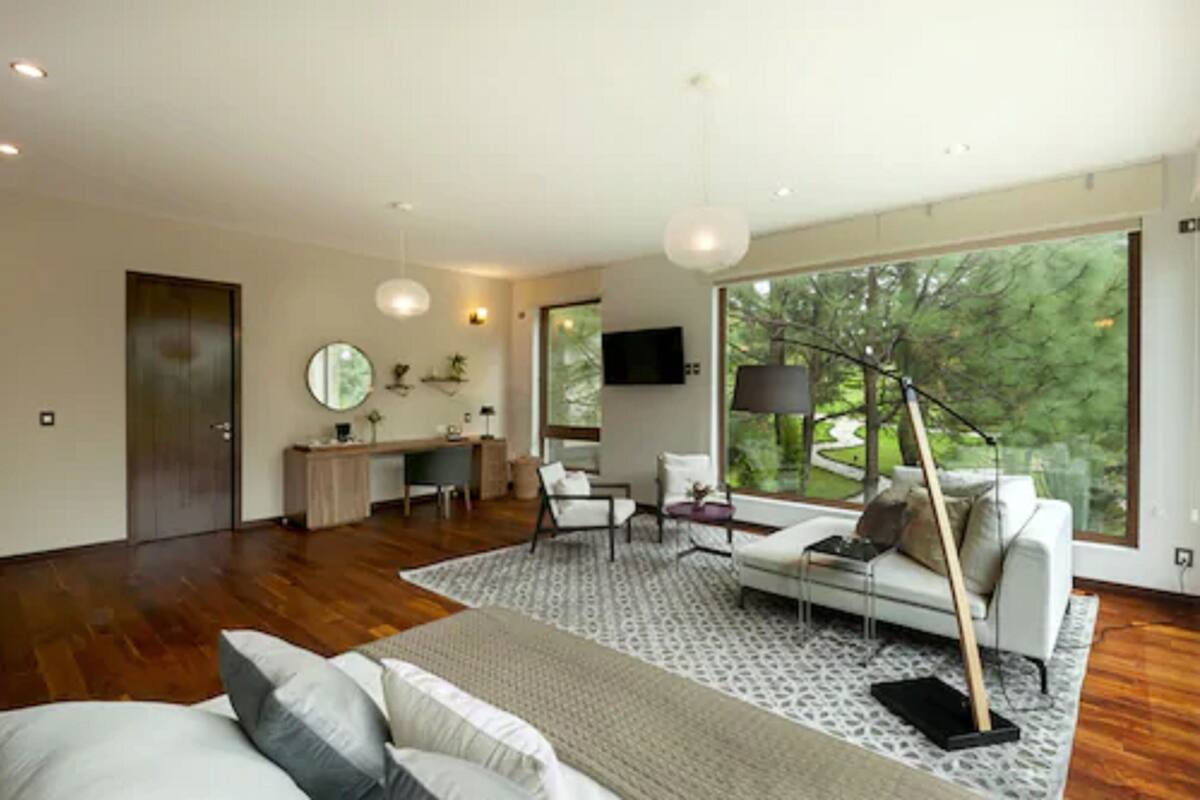 A modern living room with a large window, a sofa, a coffee table, and a desk area.